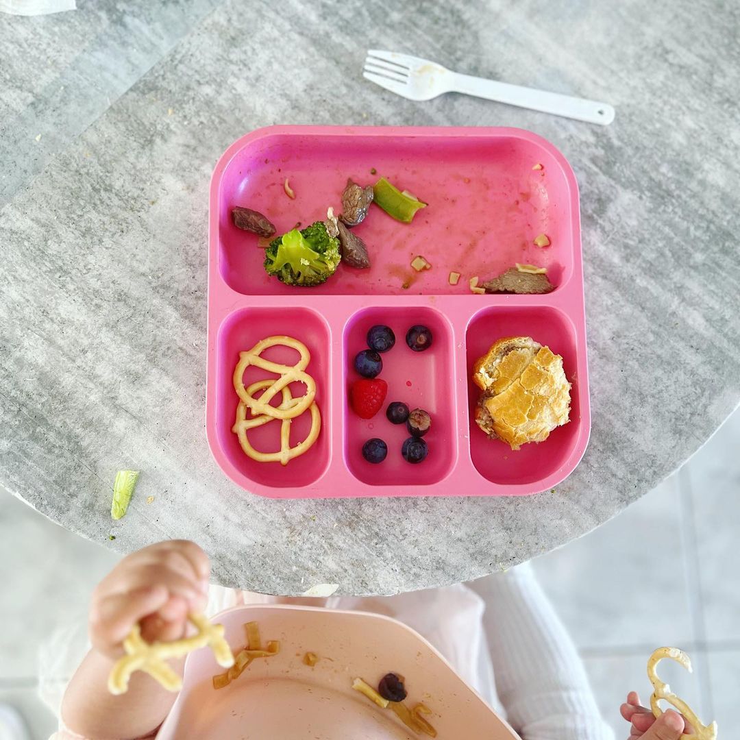 child eating from a bamboo bento plate with pretzels, blueberries and vegetables in it