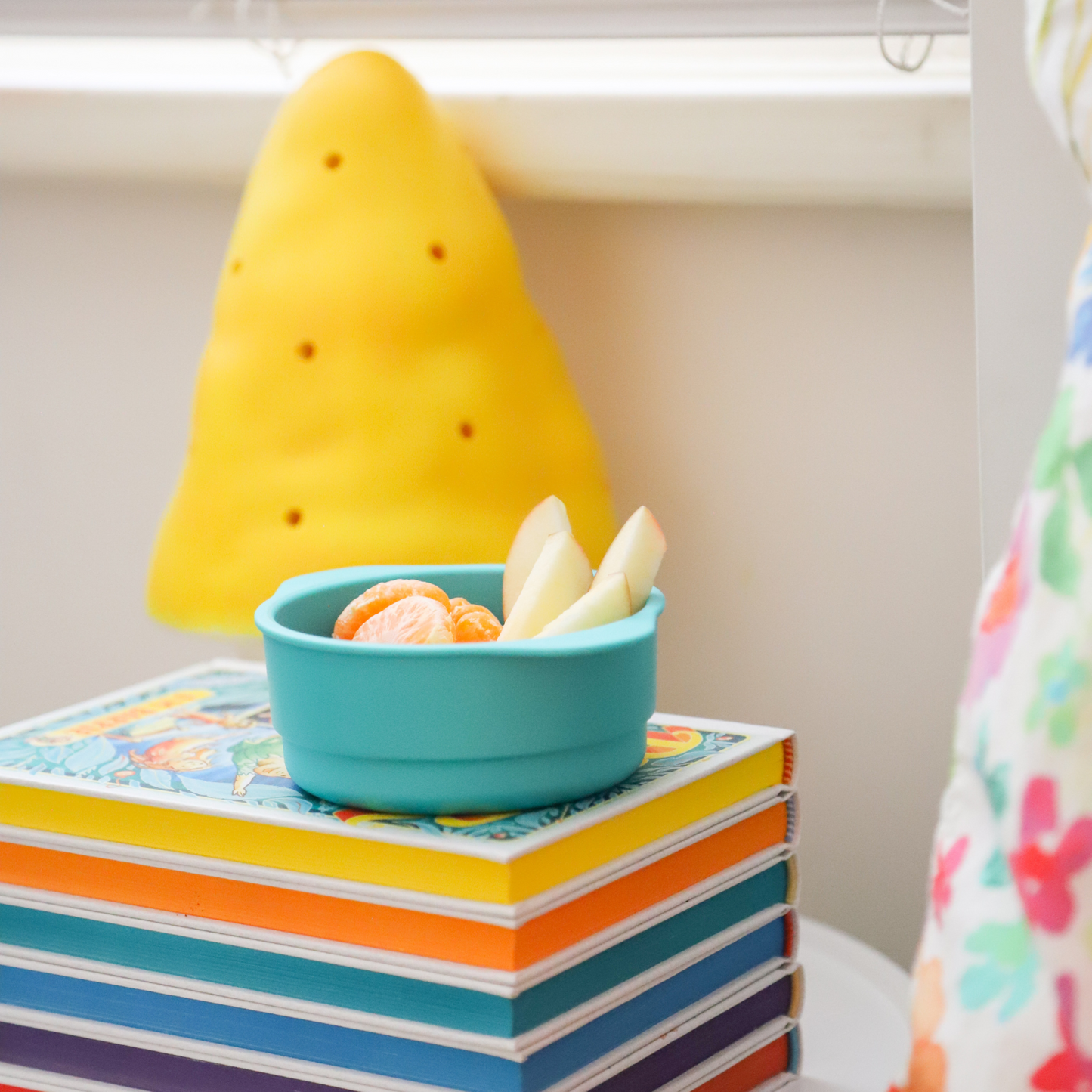 a bobo&boo snack bowl in green with apples and mandarins in them sitting on books