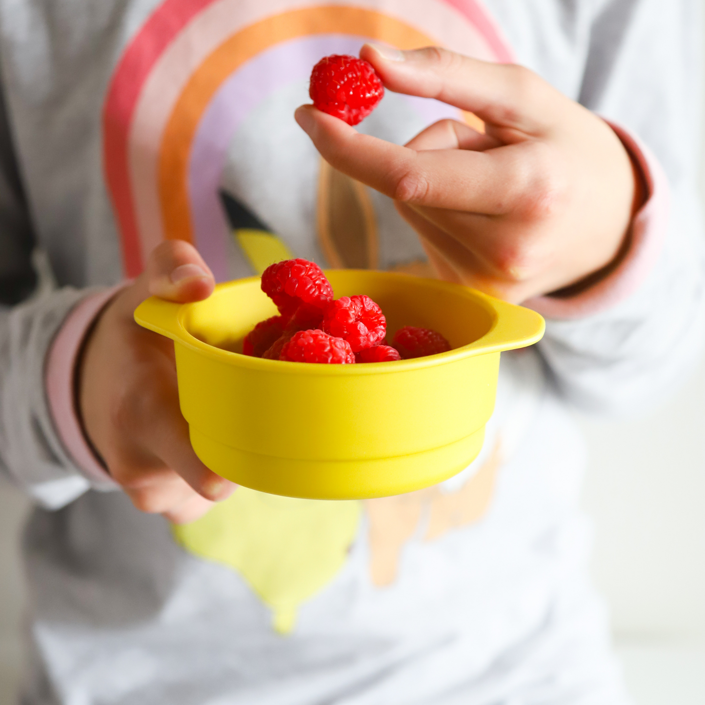 a girl eating raspberries out of bamboo snack bowls in yellow