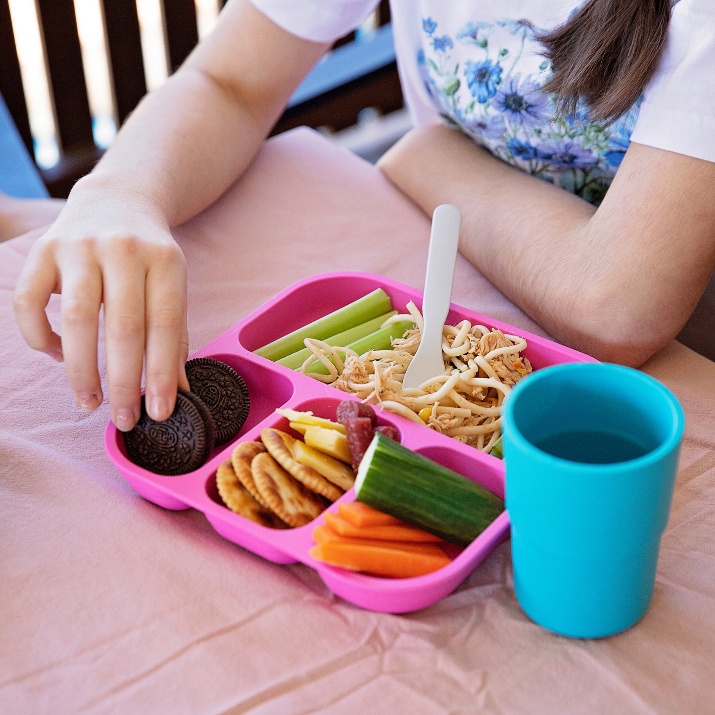 a girl eating a meal out of a bobo&boo plant-based divided plate in pink which has carrots, cucumbers, crackers & snacks